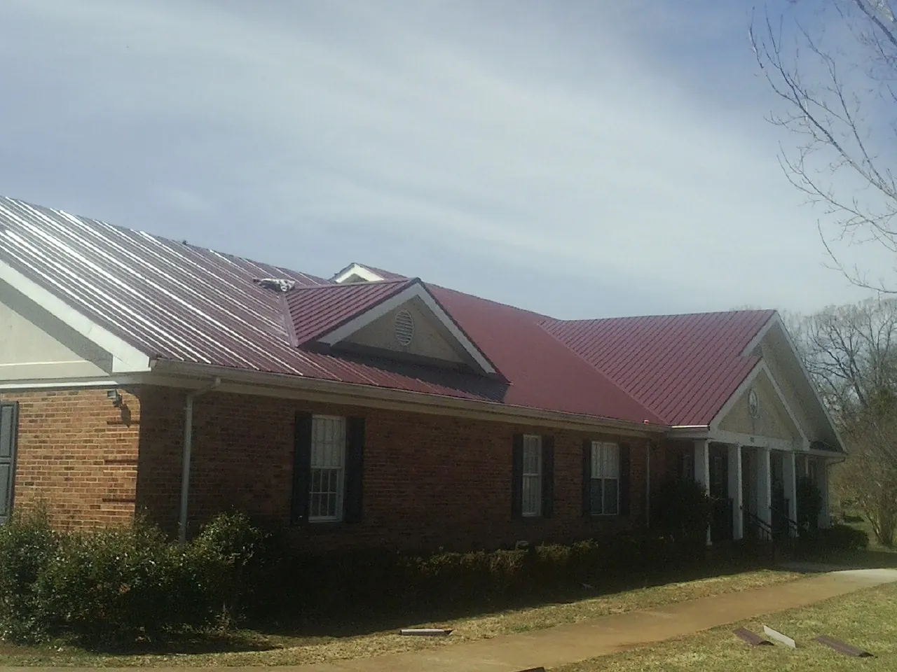 Red metal roof with gabled entries on a long brick building, from a Hail Damage Roof Repair job in Jerome