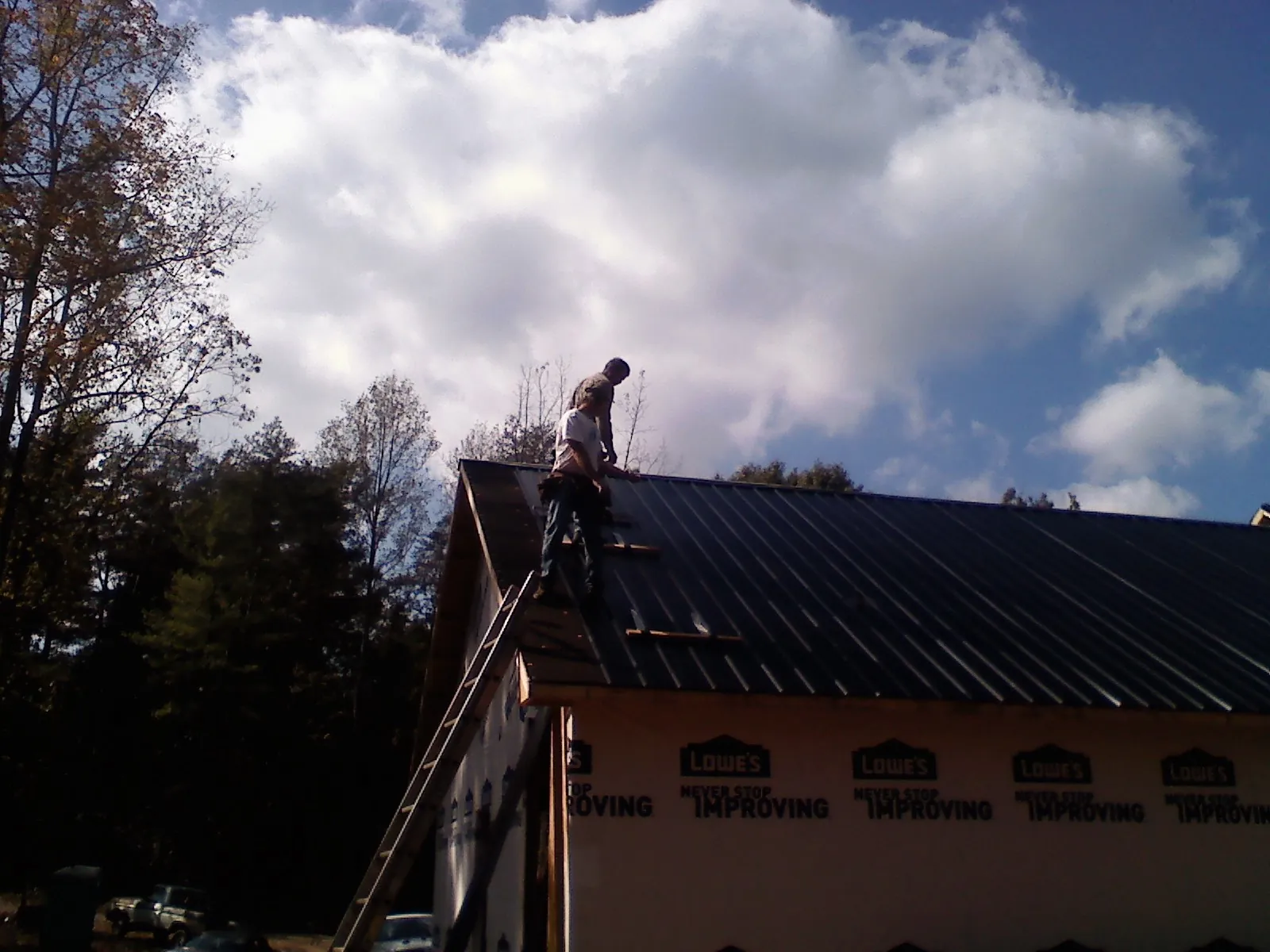 Roofer fastening dark metal panels high against a cloudy sky, from a Roof Inspection job in Jerome